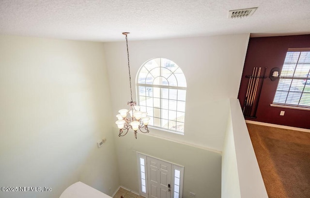 carpeted foyer entrance featuring a chandelier, a textured ceiling, visible vents, and baseboards