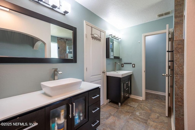 bathroom with two vanities, visible vents, a sink, and a textured ceiling