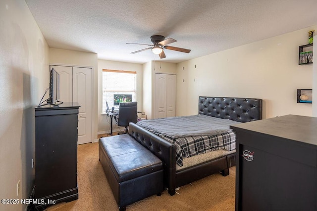 bedroom featuring light colored carpet, ceiling fan, a textured ceiling, and two closets