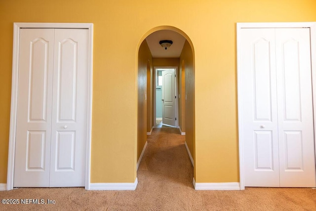 hallway featuring arched walkways, carpet, and baseboards