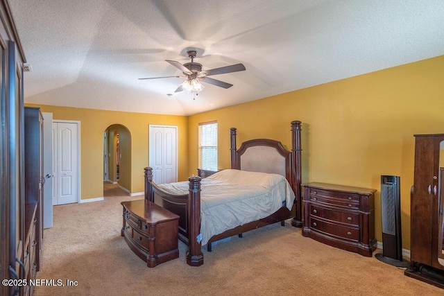 bedroom featuring arched walkways, multiple closets, light colored carpet, a textured ceiling, and baseboards