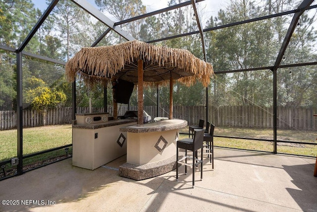 view of patio featuring glass enclosure, a fenced backyard, and outdoor dry bar