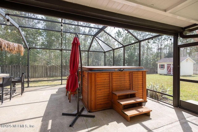 view of patio / terrace featuring an outbuilding, glass enclosure, a storage unit, and a hot tub