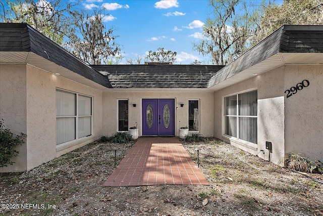 property entrance featuring a shingled roof, mansard roof, and stucco siding