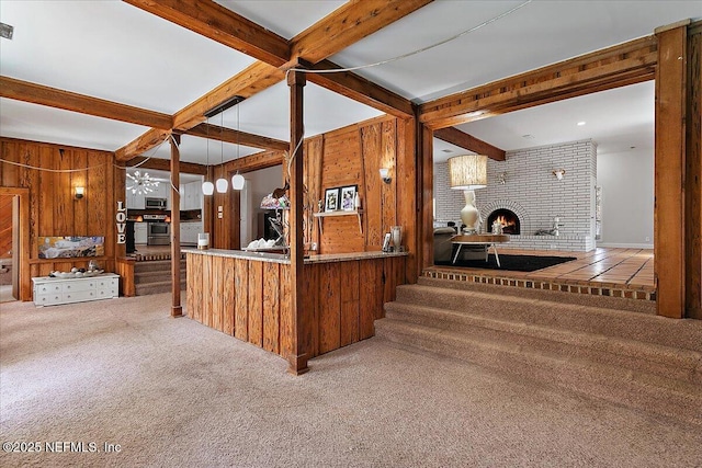 kitchen with beam ceiling, appliances with stainless steel finishes, a brick fireplace, carpet flooring, and wood walls