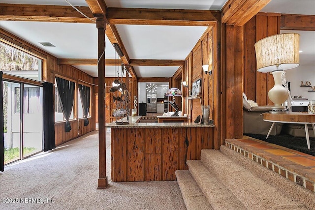 kitchen with light colored carpet, wooden walls, visible vents, beam ceiling, and brown cabinetry