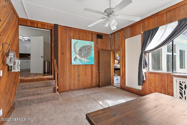 carpeted foyer entrance with ceiling fan, wooden walls, and stairway