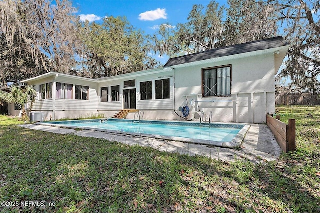 rear view of house with an outdoor pool, cooling unit, a sunroom, and a yard