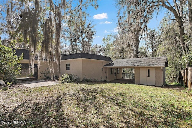 rear view of property with stucco siding, fence, and a lawn