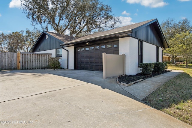 view of property exterior featuring an attached garage, fence, concrete driveway, and brick siding