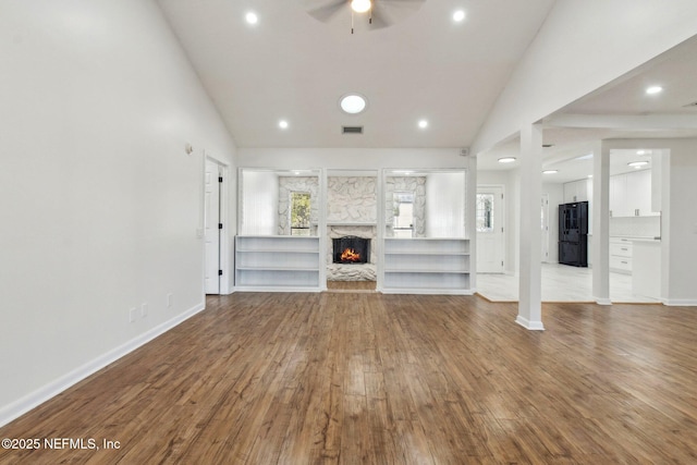 unfurnished living room featuring a warm lit fireplace, visible vents, baseboards, and wood finished floors