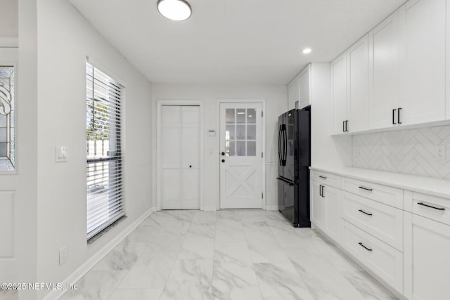 kitchen with marble finish floor, decorative backsplash, freestanding refrigerator, white cabinets, and baseboards