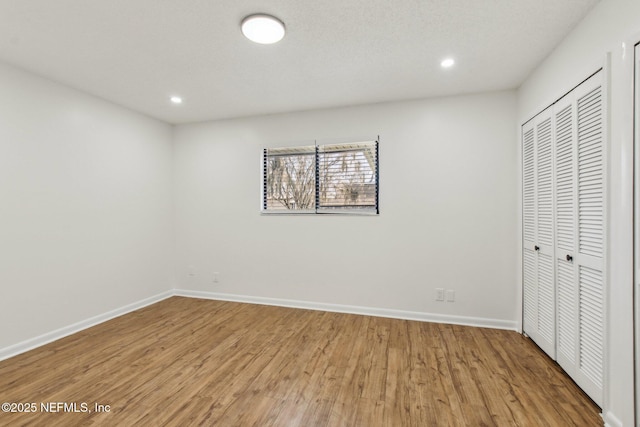 unfurnished bedroom featuring a closet, baseboards, wood finished floors, and recessed lighting