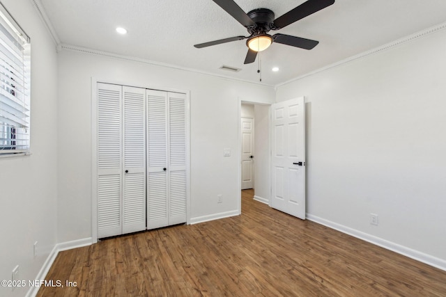 unfurnished bedroom featuring wood finished floors, visible vents, baseboards, a closet, and crown molding