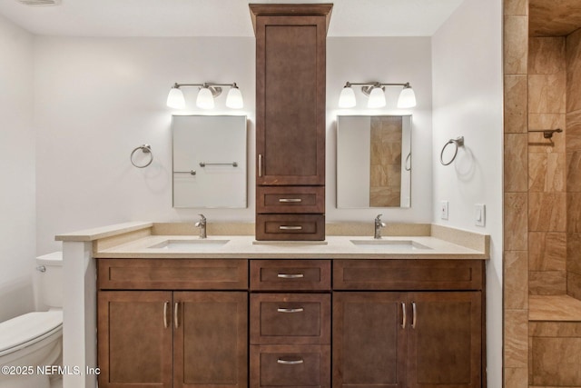 full bath featuring toilet, double vanity, a tile shower, and a sink