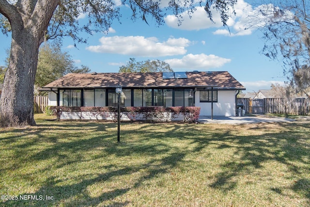 back of property with roof mounted solar panels, fence, and a lawn