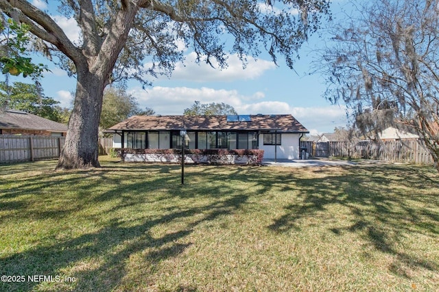 back of property with a yard, a fenced backyard, and roof mounted solar panels