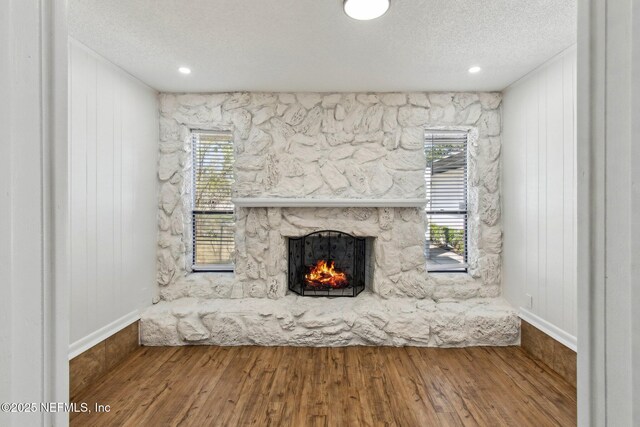 unfurnished living room featuring a textured ceiling, wood finished floors, and a stone fireplace