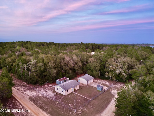 aerial view at dusk featuring a wooded view