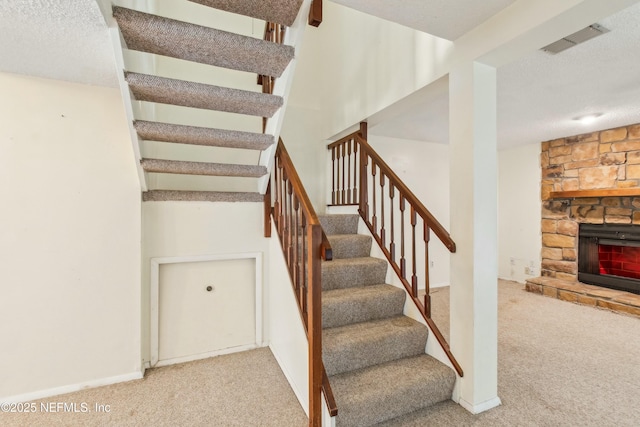 stairway with carpet, visible vents, a fireplace, and a textured ceiling