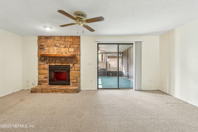 unfurnished living room with a ceiling fan, carpet flooring, a stone fireplace, and a textured ceiling