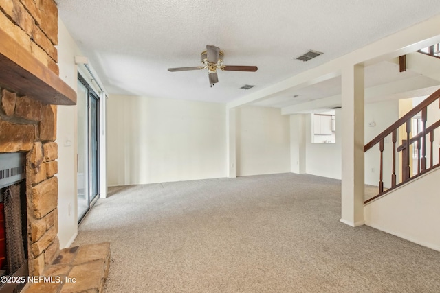 unfurnished living room featuring visible vents, stairway, a stone fireplace, a textured ceiling, and carpet flooring