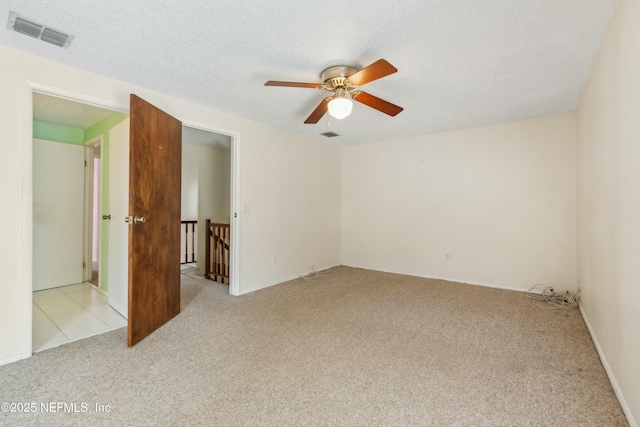 carpeted spare room with a textured ceiling, visible vents, and a ceiling fan