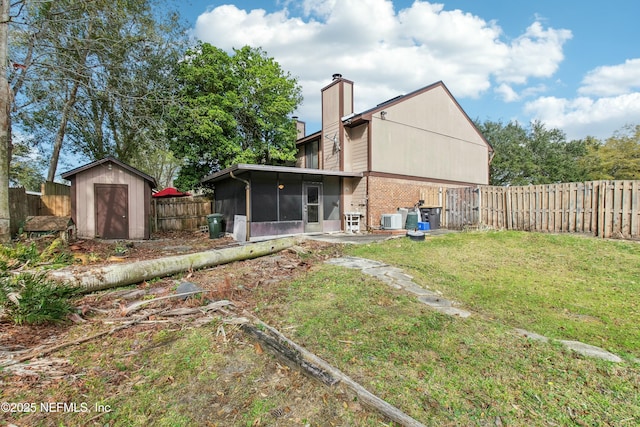 back of property with a yard, a chimney, a sunroom, a shed, and a fenced backyard