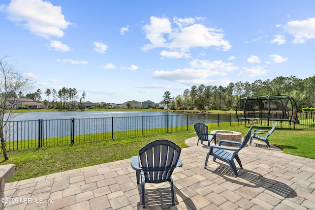 view of patio with a trampoline, a fenced backyard, a water view, and an outdoor fire pit