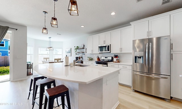 kitchen with light wood-type flooring, visible vents, stainless steel appliances, and an island with sink