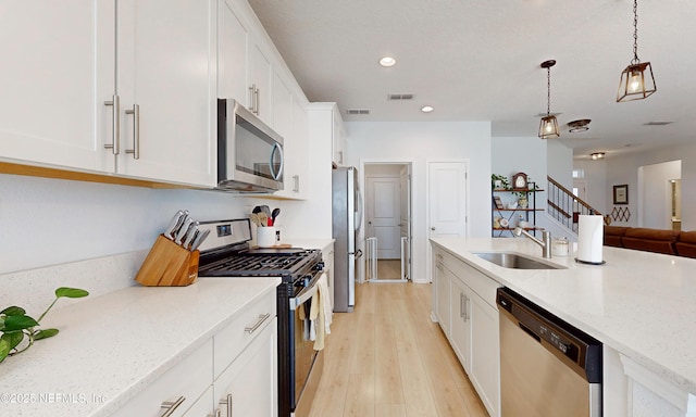 kitchen featuring stainless steel appliances, a sink, visible vents, white cabinets, and decorative light fixtures