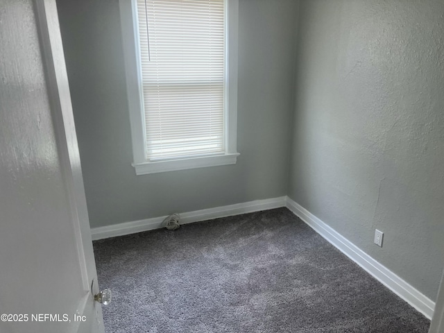 unfurnished room featuring baseboards, dark colored carpet, and a textured wall