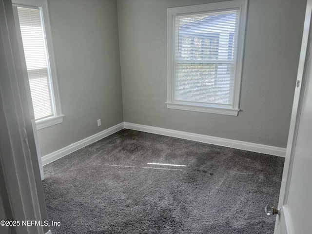 empty room with a textured wall, a wealth of natural light, dark carpet, and baseboards