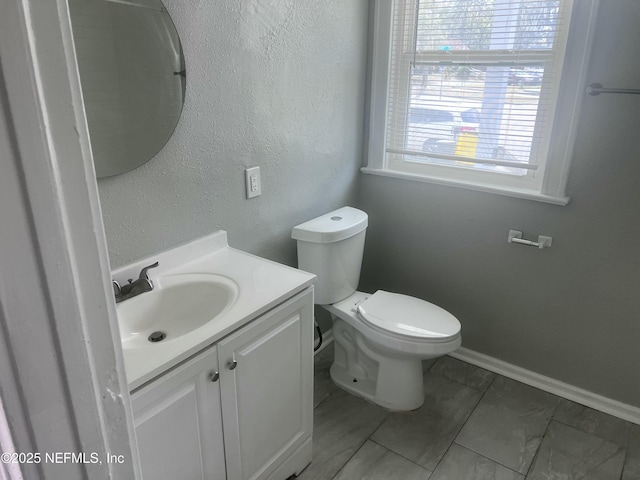 bathroom featuring toilet, a textured wall, baseboards, and vanity