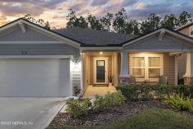 craftsman-style house featuring a shingled roof, covered porch, concrete driveway, a garage, and stone siding