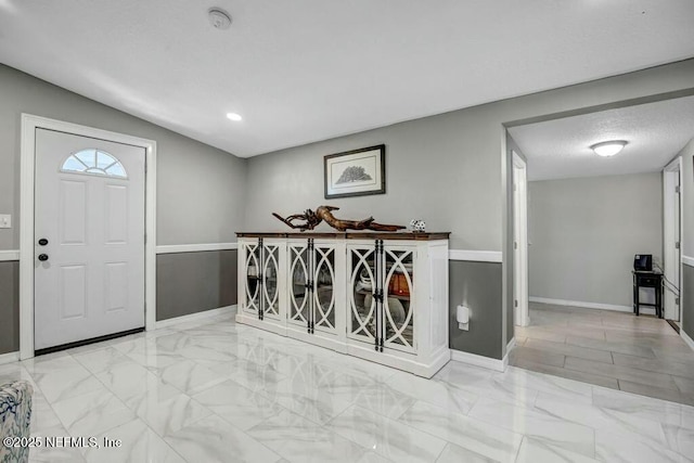 foyer entrance featuring marble finish floor, a textured ceiling, and baseboards