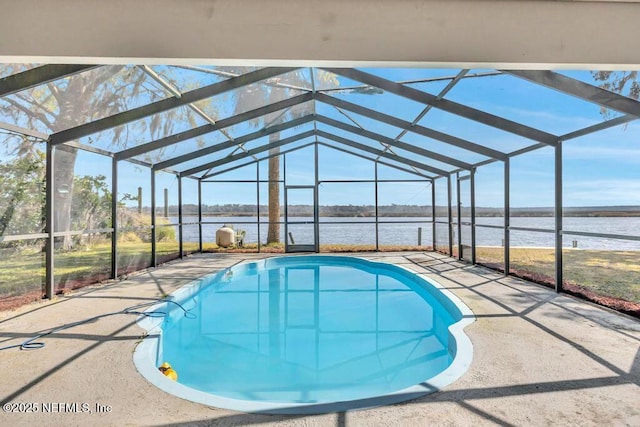 pool featuring glass enclosure, a patio, and a water view