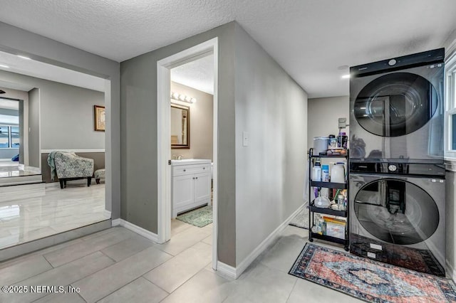 washroom with a textured ceiling, laundry area, stacked washing maching and dryer, and baseboards