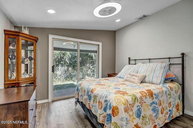 bedroom featuring a textured ceiling, wood finished floors, visible vents, baseboards, and access to outside