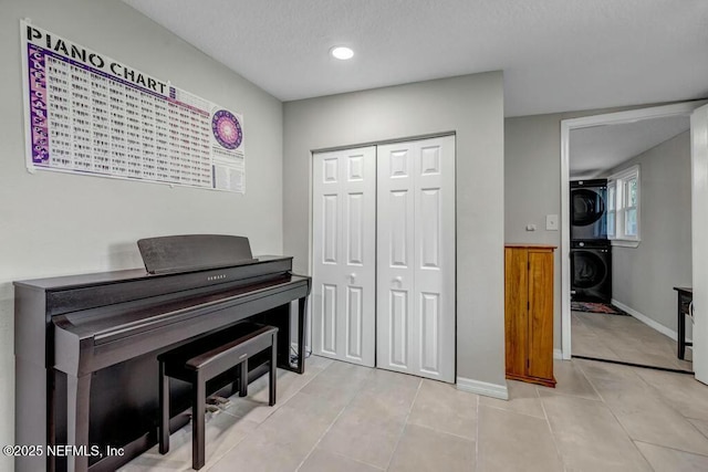 sitting room featuring stacked washer / dryer, a textured ceiling, baseboards, and light tile patterned floors