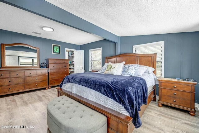 bedroom with a spacious closet, a textured ceiling, visible vents, and wood finished floors