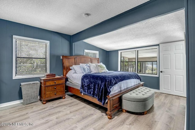 bedroom featuring a textured ceiling, multiple windows, baseboards, and wood finished floors