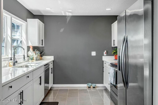 kitchen featuring stainless steel appliances, light countertops, white cabinets, a sink, and baseboards