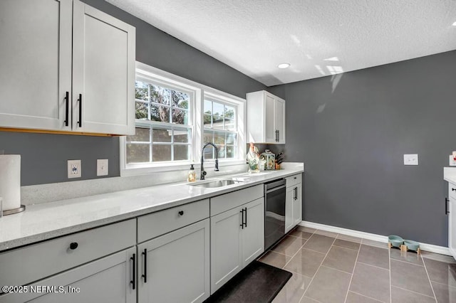 kitchen with light tile patterned flooring, a sink, a textured ceiling, dishwasher, and baseboards