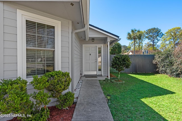 view of exterior entry with a yard and fence