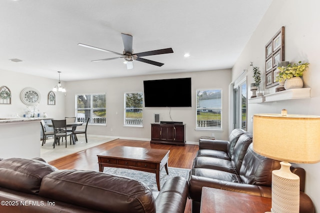 living room featuring ceiling fan with notable chandelier, baseboards, wood finished floors, and a healthy amount of sunlight