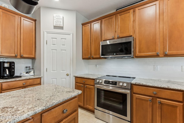 kitchen featuring tasteful backsplash, appliances with stainless steel finishes, light stone counters, and brown cabinets