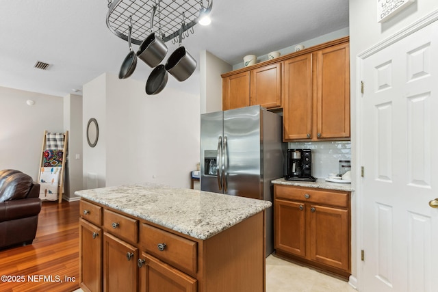 kitchen with stainless steel fridge, visible vents, brown cabinetry, a kitchen island, and backsplash