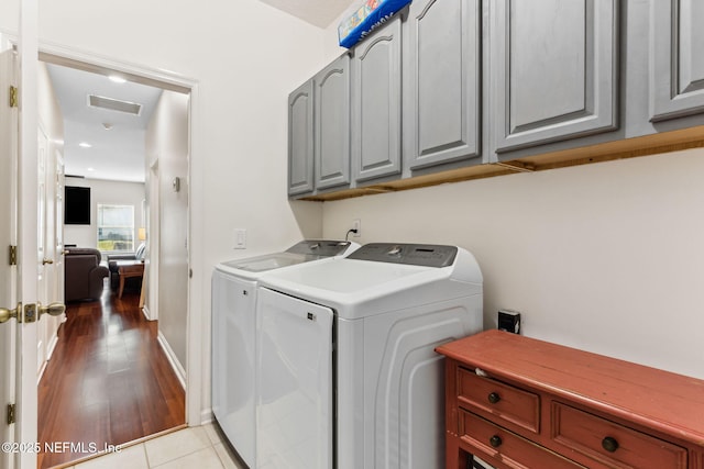 washroom with visible vents, washer and clothes dryer, light wood-type flooring, and cabinet space