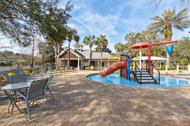 community jungle gym featuring a patio area, a water play area, fence, and a community pool